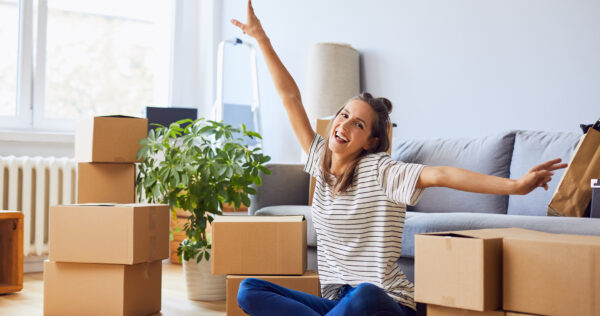 Young woman sitting in new apartment and raising arms in joy after moving in